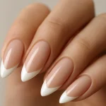 Close-up of almond-shaped nails with nude base and white tips, studio lighting