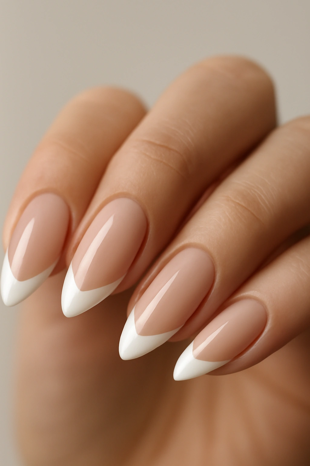 Close-up of almond-shaped nails with nude base and white tips, studio lighting