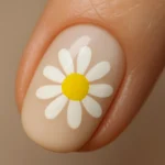 Close-up of a fingernail with white petals and yellow center in a daisy dot design