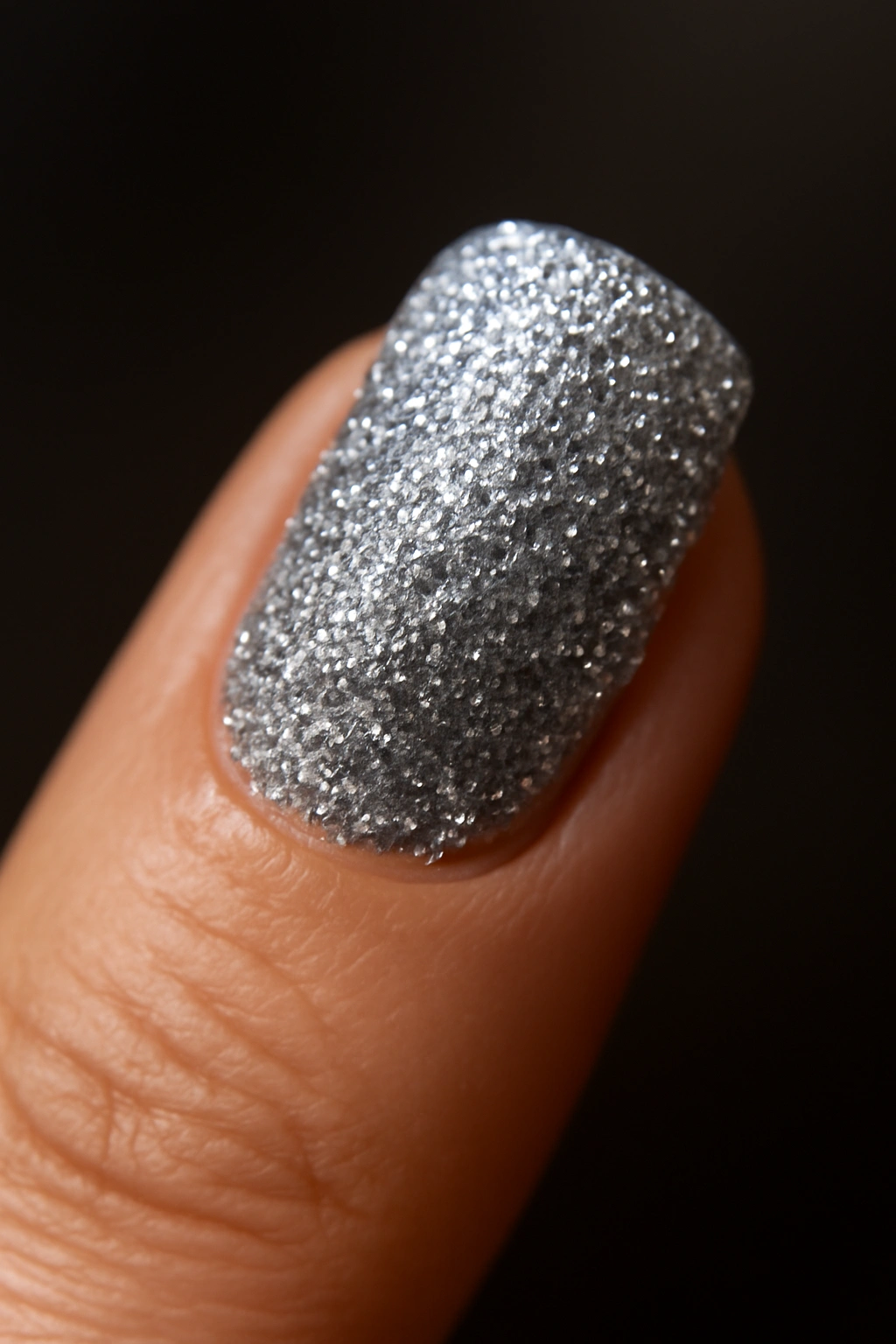 Close-up of a glitter nail with silver glitter on a dark background