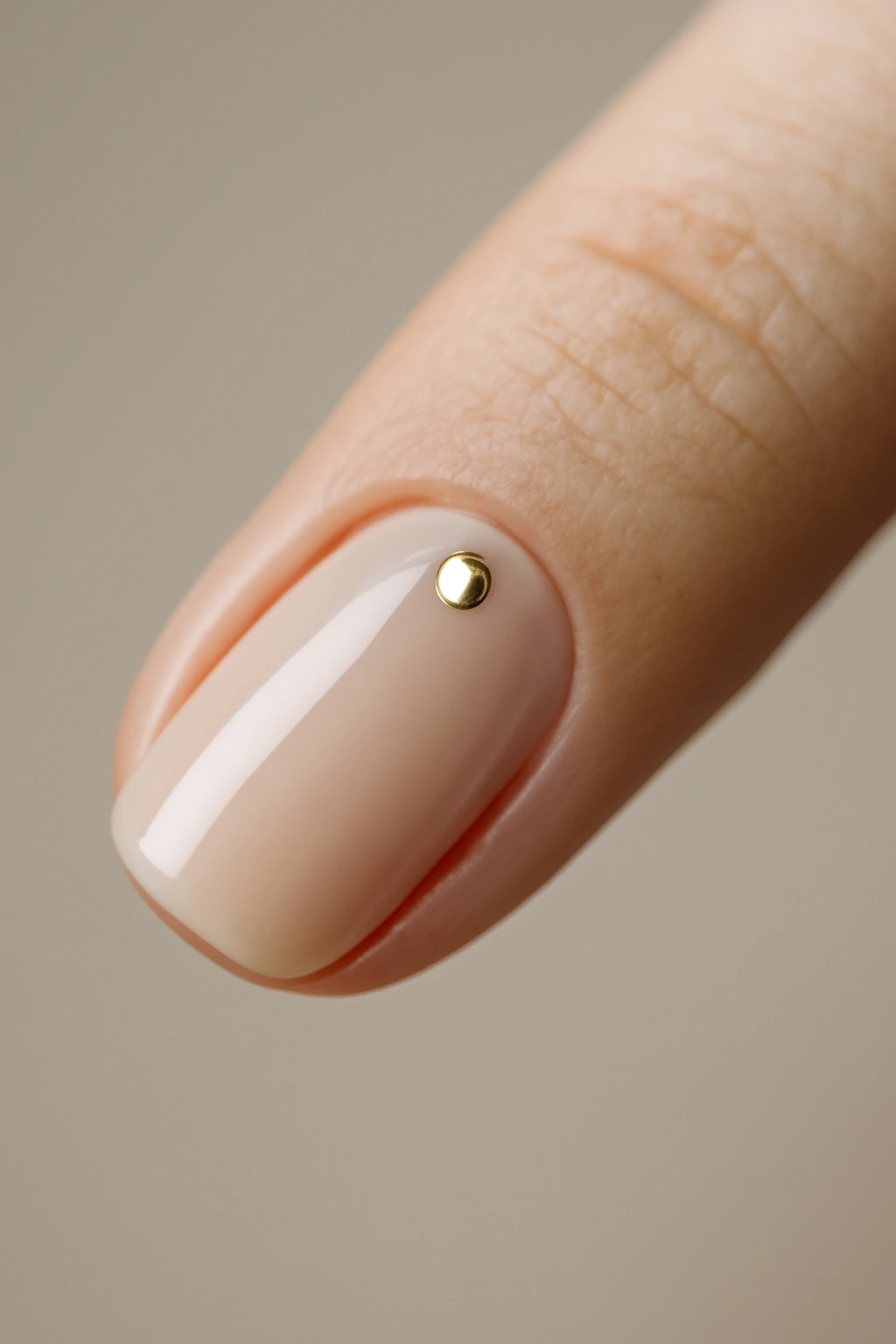 Close-up of a single nude nail with a small metallic stud
