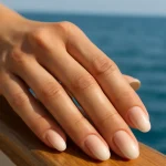 Close-up of hand with soft ombre French manicure on yacht deck
