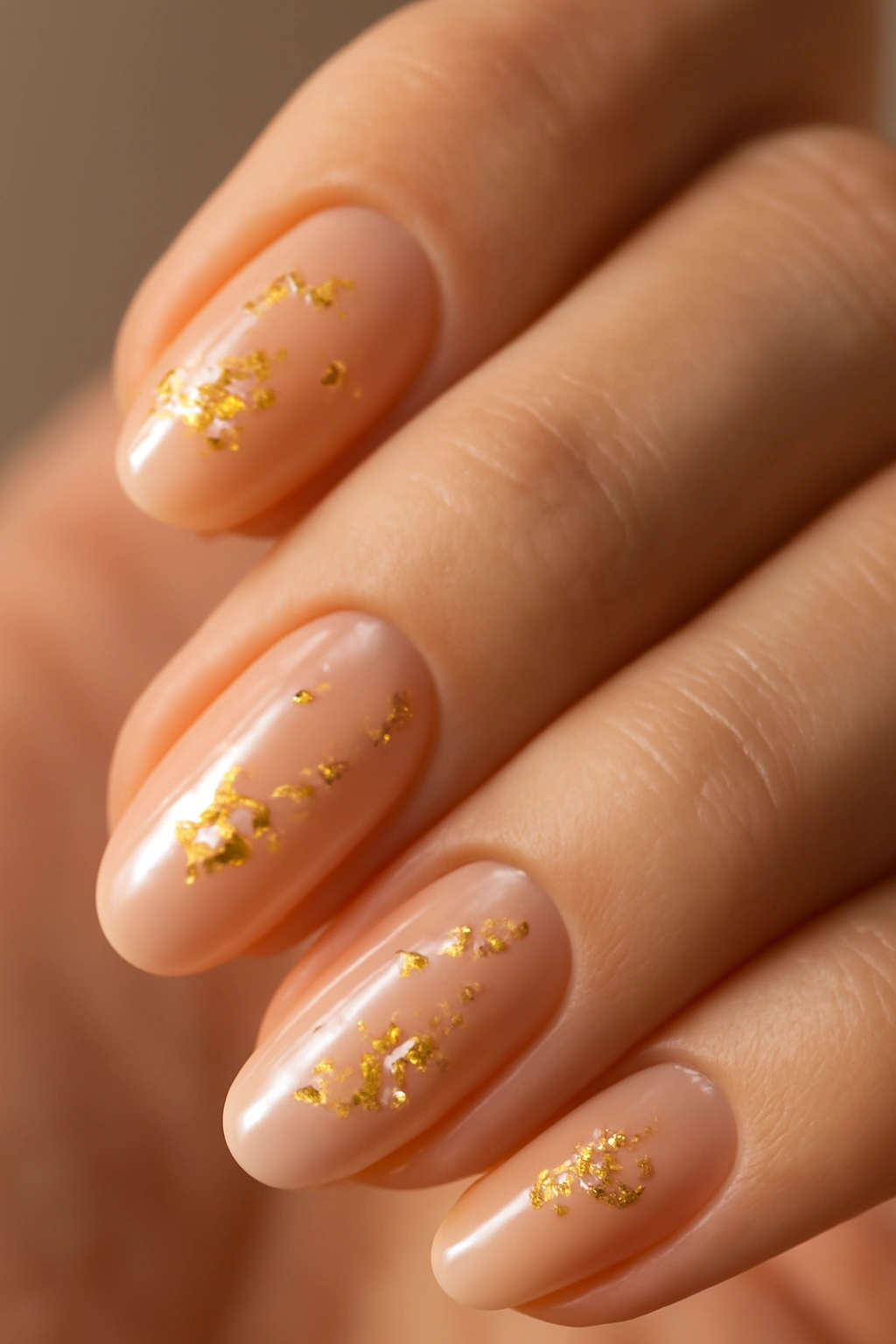Close-up of hands with nude nails accented by irregular gold foil